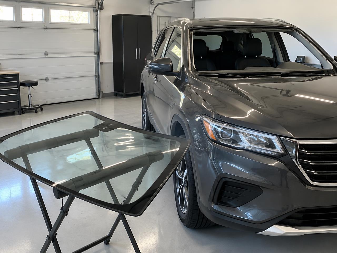 Voiture dans un garage propre avec un pare-brise neuf posé sur un support